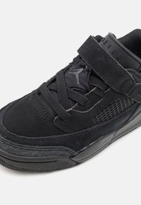 Baskets noires en suède et mesh, avec un design à lacets et une sangle, semelle texturée et panneau latéral perforé.