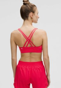 Sujeción deportiva rosa con tirantes entrecruzados, combinada con pantalones cortos rosa de corte holgado. Tejido suave y elástico. Detalle de marca mínimo.