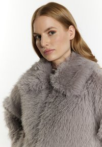 Cappotto in finta pelliccia grigia con una morbida texture e un ampio colletto. Il tessuto presenta lunghe fibre soffici che creano una silhouette voluminoso.