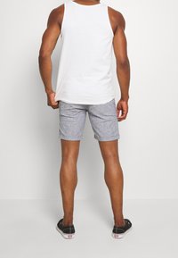 Bílý tílko, šedo-bílé pruhované kraťasy, ke kolenům. Kraťasy mají ohrnutý lem a jsou nošeny s černými nazouvacími botami.