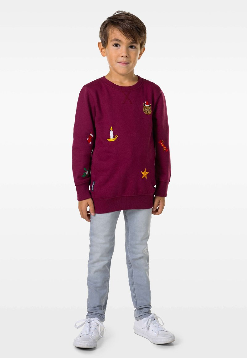 Bordeauxfarbener Sweatshirt mit bestickten Verzierungen, darunter eine Katze, eine Kerze und Sterne; hat lange Ärmel und eine lockere Passform. Getragen mit hellblauen Jeans.