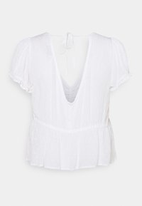 Blouse blanche avec manches courtes bouffantes, dos en V profond, tissu texturé avec petits points, et taille froncée pour une coupe évasée.