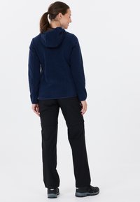 Mörkblå fleecejacka med huva och en texturerad design. Matchad med svarta cargobyxor och grå vandringsskor, sedd bakifrån.