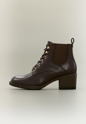 Bottine en cuir marron foncé avec lacets à l'avant, panneau latéral élastique, languette au talon et petit talon bloc sur un fond clair uni.
