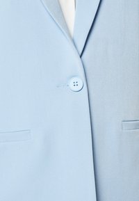 Blazer azul claro con una textura suave, solapas de muesca y cierre de botón simple. Presenta dos bolsillos frontales y detalles de costura limpios.