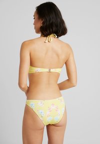 Žlté kvetinové bikiny s nastaviteľným viazaním za krkom, ktoré majú malé ružové a modré kvety, elastický materiál a sponu na zadnej strane vrchného dielu.