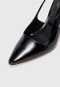 Pantofii slingback din piele vernis neagră au un vârf ascuțit și un design elegant. Prezintă o suprafață lucioasă și un toc deschis, oferind o siluetă modernă.