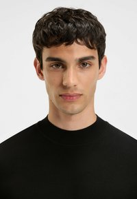 Schwarzer, gerippter Rundhals-Pullover aus einem glatten Strickstoff. Eng anliegende Silhouette mit minimalen Nähten, die ein einfaches Design präsentiert.