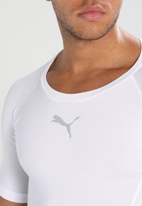 Hvitt treningsshirt laget av glatt, stretchmateriale med korte ermer, som har en subtil grå Puma-logo på brystet.