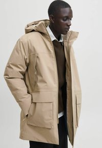 Bežna vodoodporna parka jakna s kapuco, ki ima zadrgo in sproščen kroj. Gladka tekstura in minimalistični oblikovalski elementi.