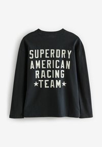 Tricou negru cu mânecă lungă, prezentând text imprimat alb "SUPERDRY AMERICAN RACING TEAM" cu stele, realizat din țesătură de bumbac, croială standard.