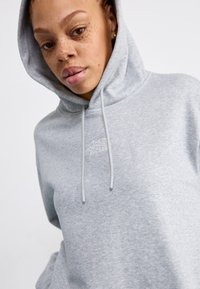 Grijze hoodie gemaakt van zachte stof; heeft een voorzak, koordjes en geborduurd logo boven de zak.