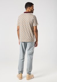 Lyhyttailoinen polo-paita, jossa on sydänkuvio vaaleanbeigeinä ja vaaleansinisinä, sekä tummanpunainen kaulus. Yhdistetty vaaleanharmaisiin slim-fit-housuihin ja beigeihin lenkkareihin.