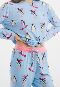Světle modrý pyžamový set se tučňáky na lyžích. Měkká, elastická látka s růžovým pasem a šňůrkou, dlouhé rukávy a zábavný vzor.