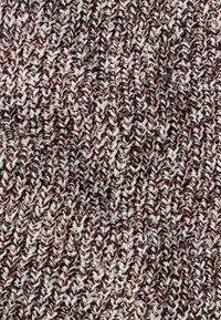 Pletená textília s kombináciou krémových, červených a čiernych vlákien, s textúrovaným vzorom. Mäkký a pružný materiál, ktorý zobrazuje tkaný dizajn.