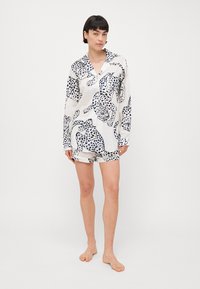 Leichtes, kurzärmliges Pyjama-Set aus glattem Material, mit weißem Grund und schwarzem Leopardenmuster sowie kontrastierenden Akzenten an den Shorts.