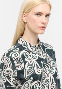 Long-sleeved shirt featuring a swirling abstract pattern in dark green, cream, and black, with a button-down collar and soft fabric texture.
