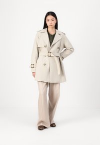 Beige trenchcoat med dobbeltspent knapper, belted midje og skulderklapper, sammen med beige bredde bukser og leopardskledde sko.