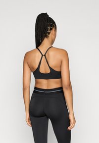 Fekete sportmelltartó keresztpántokkal a hátoldalon, rugalmas anyagból készült. Kulcslyuk dizájnnal rendelkezik, és magas derekú fekete leggingsszel van párosítva.