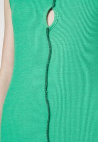 T-shirt verde de alças com detalhe cortado verticalmente e costura preta. O tecido é suave e tem um corte ajustado.