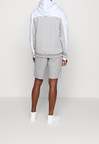 Felpa grigia e bianca con una vestibilità morbida e una tasca a marsupio, abbinata a pantaloni corti grigi, indossata con sneakers bianche alte.
