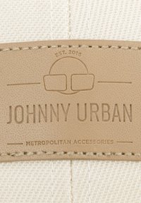 Beige szövetcímke, domború betűzéssel, amelyen a "JOHNNY URBAN" felirat olvasható, szemüveg ikon mellett az "METROPOLITAN ACCESSORIES" felirattal alatta. Tartós anyag.