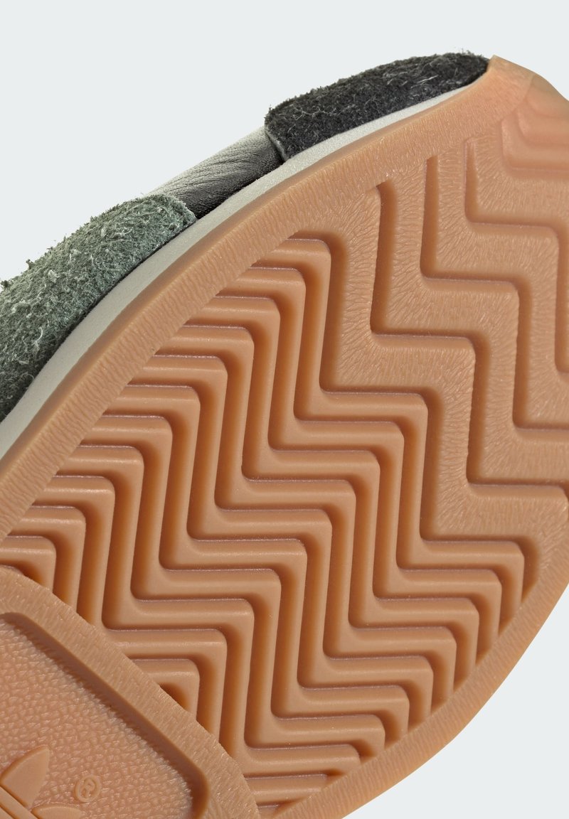 Zielone zamszowe i czarne skórzane sneakersy z teksturowaną, brązową gumową podeszwą o wzorze zygzaka oraz detalem z logo na pięcie.