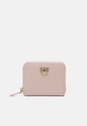 Portafoglio in pelle rosa compatto con un accento di emblema dorato, chiusura con zip e piccolo anello per fissarlo. Texture liscia, forma rettangolare.