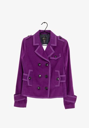 Lila Damenblazer mit doppelreihiger Knopfleiste, schwarzen Knöpfen, Reverskragen, geknöpften Pattentaschen und dekorativen Schulterpatten an einem Bügel.