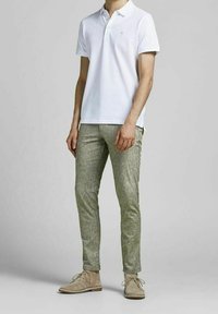 Biała koszulka polo z krótkim rękawem i kołnierzykiem, zestawiona z jasnymi zielonymi, teksturowanymi, dopasowanymi spodniami oraz beżowymi zamszowymi butami typu desert boots.