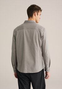 Camisa de hombre de manga larga en gris claro, tela texturizada, con cuello puntiagudo y puños con botones; diseño trasero de corte recto.