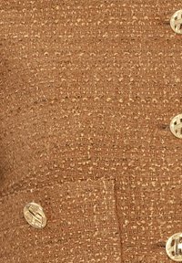 Gros plan sur un tissu marron texturé avec des boutons ronds dorés présentant un motif géométrique imbriqué.