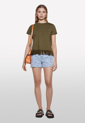 T-shirt en coton vert olive avec un ourlet à frange, associé à un short en denim brodé bleu clair et des sandales à plateforme noires. Accessoire de sac orange.