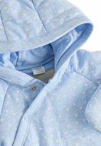 Jasnoniebieska bluza z kapturem w gwiazdy, wykonana z miękkiego materiału. Wyposażona w zapięcia na napy oraz okrągły kołnierz. Zawiera podszewkę w kapturze.