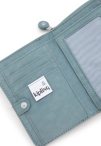 Světle modrá látková peněženka s několika kapsami na karty, průhledným oknem na ID a zacvakávacím uzávěrem. Obsahuje štítek s logem Kipling.