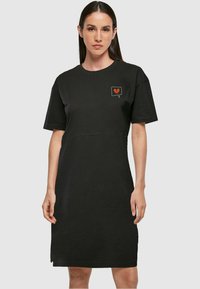 Fekete pamut T-shirt ruha rövid ujjakkal, kis piros szív grafikával a mellrészen és laza fazonnal. Sima textúra.