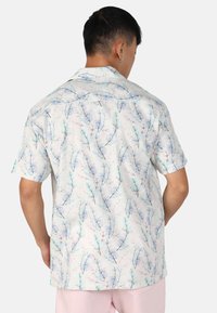 Chemise à manches courtes, à boutons, fabriquée dans un tissu léger, avec un fond clair orné de motifs de feuilles colorées et délicates.