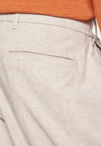 Lys beige linnedbukser med en struktureret vævning, der har en enkelt baglomme og en skræddersyet design. Fremhævet af en subtil glans.