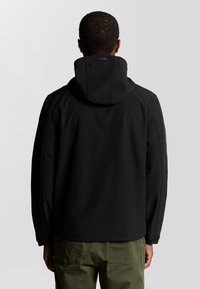 Veste à capuche noire avec une texture lisse et une coupe ajustée, dotée d'un col haut et de poignets élastiques, associée à un pantalon vert olive.