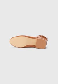 Chaussure en cuir marron à talons avec un bout arrondi et un petit talon carré. La semelle est lisse et de couleur claire, avec des accents en relief pour le grip.