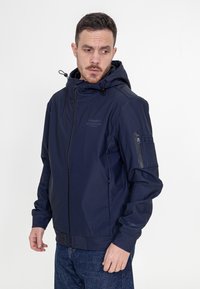 Granatowa kurtka zapinana na zamek z kapturem, wykonana z gładkiego materiału. Posiada logo na piersi oraz zasuwaną kieszeń na rękawie.