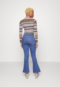 Top de manga longa, ajustado, com riscas multicoloridas em rosa, preto e amarelo; combinado com jeans azuis de cintura alta e boca de sino.