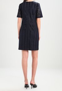 Abito navy con tessuto trasparente e perforato, maniche corte e zip sul retro. L'orlo arriva sopra il ginocchio e presenta un motivo texturizzato.