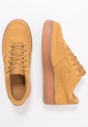Par beige ruskindssneakers med snørebånd, perforeret tå og gennemsigtige gummisåler, vist fra top- og sidevisninger på en hvid baggrund.