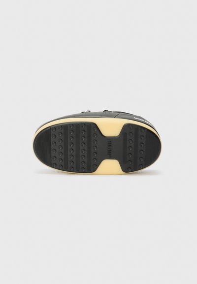 Semelle de basket noire avec une surface en caoutchouc texturé, des grips circulaires et un accent de marque. Présente une semelle intermédiaire en caoutchouc jaune contrastant.