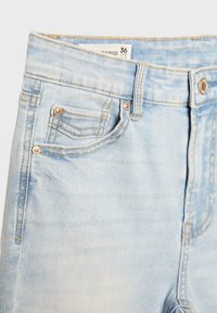 Ljust blå jeans i denim med framknapp, bältesöglor, framficka och storleksetikett som visar 36/USA 04 synlig vid midjebandet.