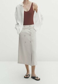 Lichtbeige linnen midi-rok met dubbelknospel; gecombineerd met een bruine tanktop en een losse witte blouse; zwarte flip-flops.