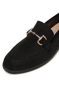 Czarne zamszowe mokasyny z akcentem w złotym kolorze, z przeszyciami i zaokrąglonym czubkiem. Płaska podeszwa dla klasycznego wyglądu.