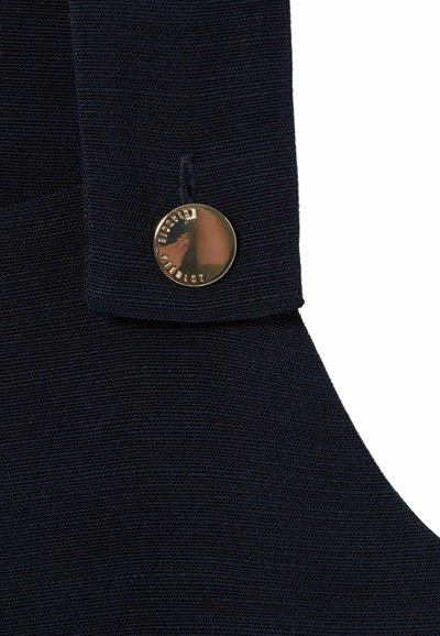 Tessuto blu navy con una finitura testurizzata, caratterizzato da un bottone metallico rotondo con una superficie riflettente e testo inciso su un lato.