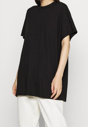 T-shirt nera oversize con texture a coste, scollatura tonda e maniche corte, abbinata a pantaloni chiari.